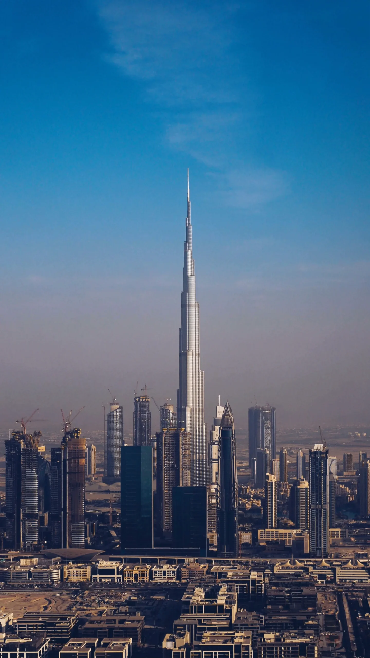 Burj Khalifa Height in Perspective: How Tall is the World's Tallest Building? A panoramic view of the Burj Khalifa, the tallest building in the world, rising majestically against a clear blue sky in Dubai, UAE, surrounded by other skyscrapers.