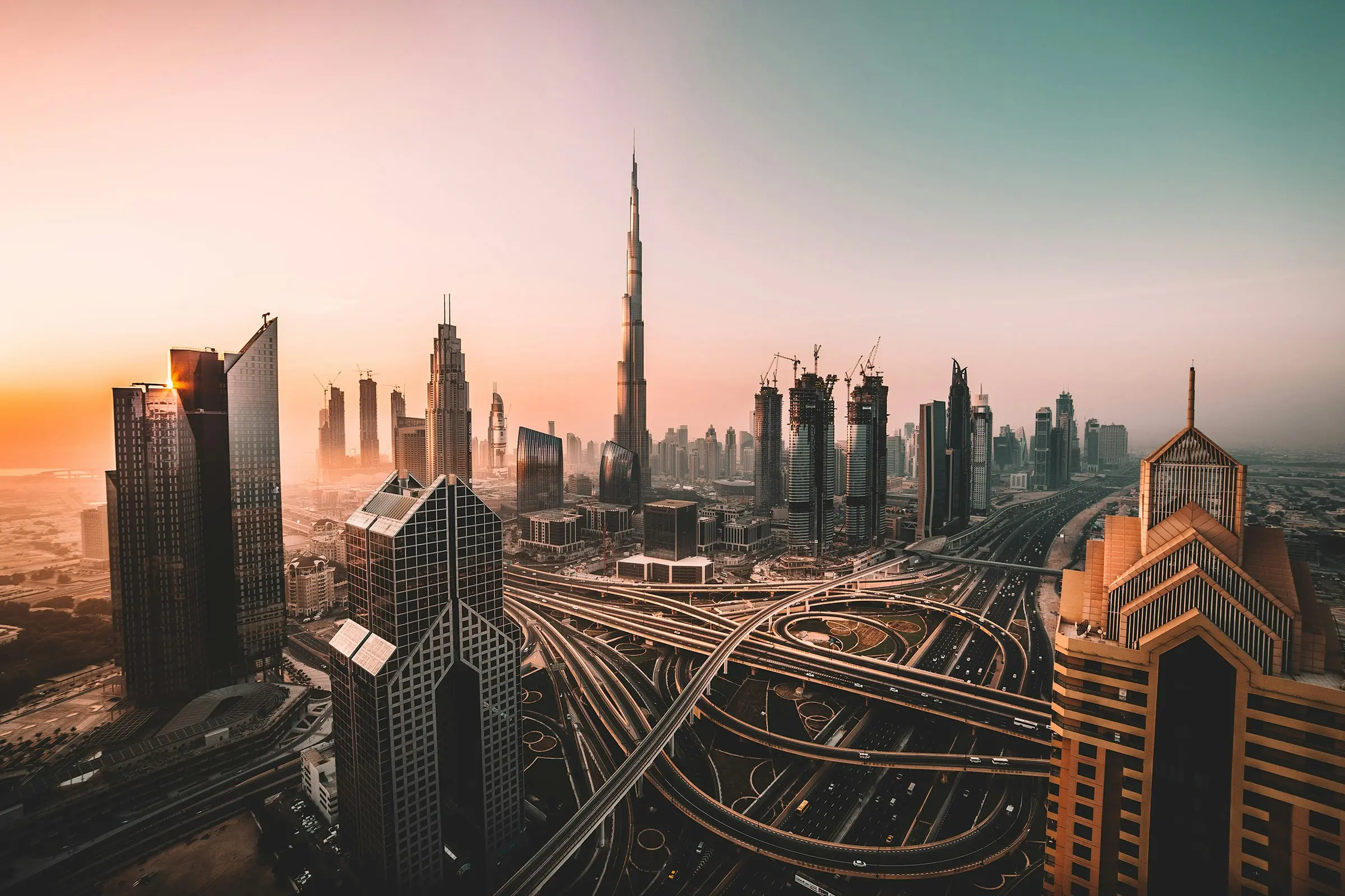 10 Tallest Buildings in the World (2025) Aerial view of Dubai's skyline showcasing the Burj Khalifa in the center, surrounded by modern buildings and highways, during sunset.