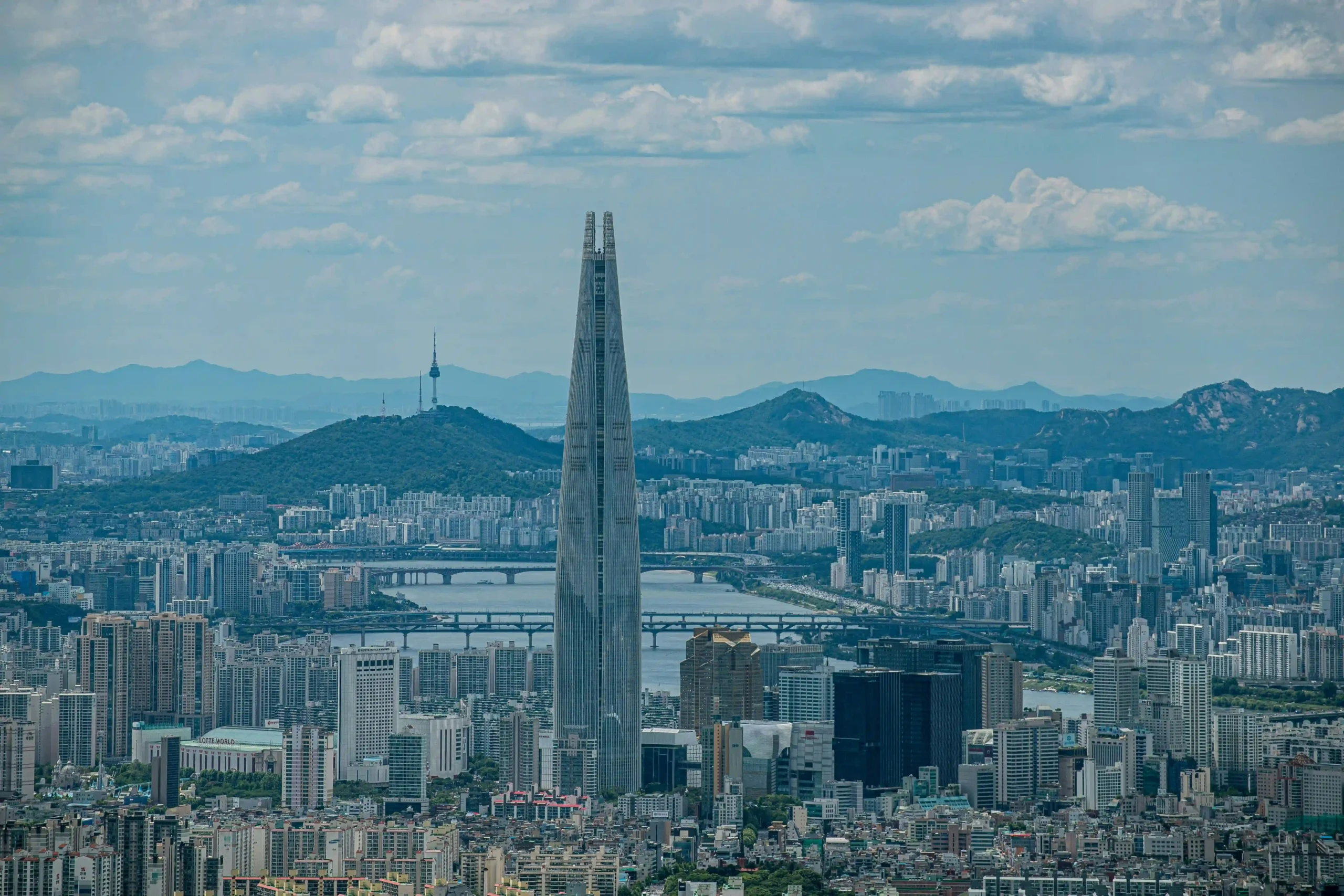 10 Tallest Buildings in the World (2025) A panoramic view of the Lotte World Tower in Seoul, South Korea, standing tall among a sprawling urban landscape, with mountains and a river in the background.