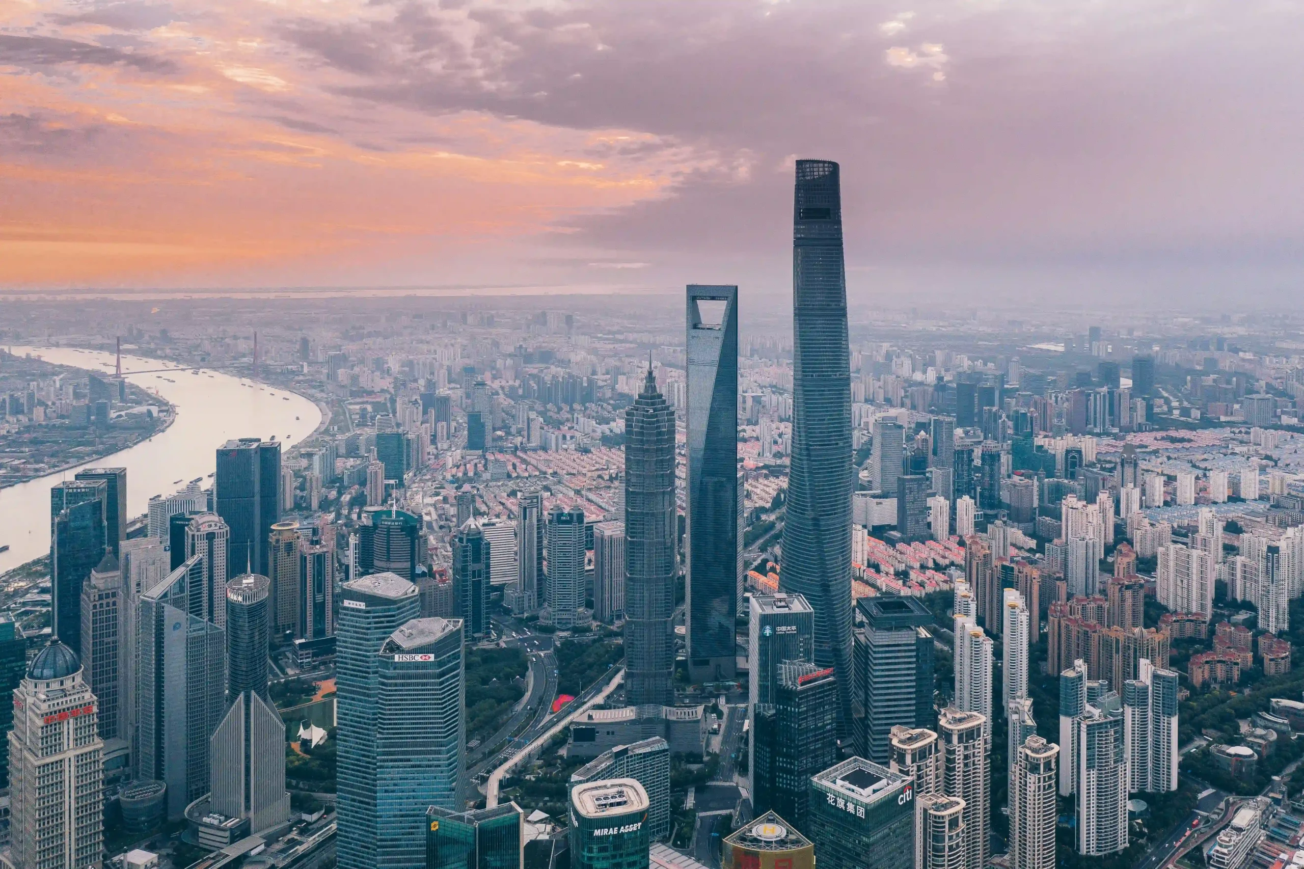 10 Tallest Buildings in the World (2025) Aerial view of Shanghai's skyline featuring the iconic Shanghai Tower, alongside other skyscrapers and the Huangpu River under a sunset sky.