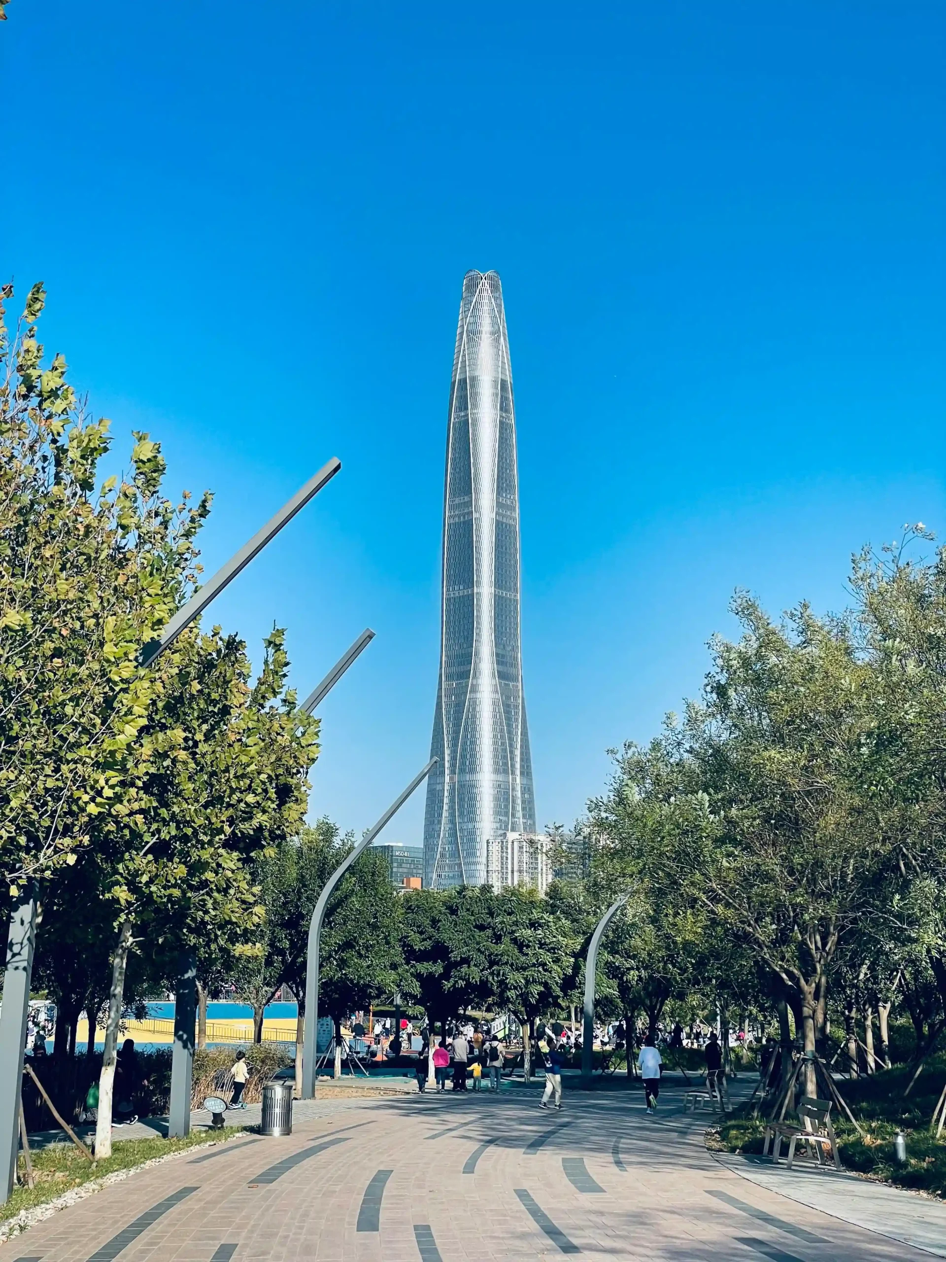 10 Tallest Buildings in the World (2025) Tianjin CTF Finance Center towering over a park with trees and clear blue sky in Shenzhen, China.